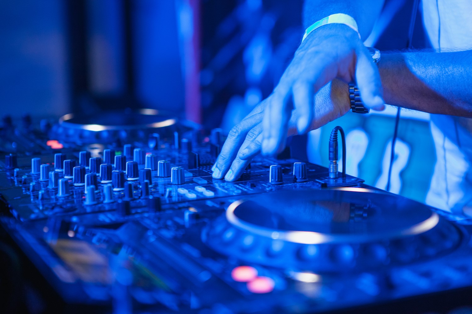 Mâini pe un mixer DJ, între două jog wheel-uri, în lumină albastră