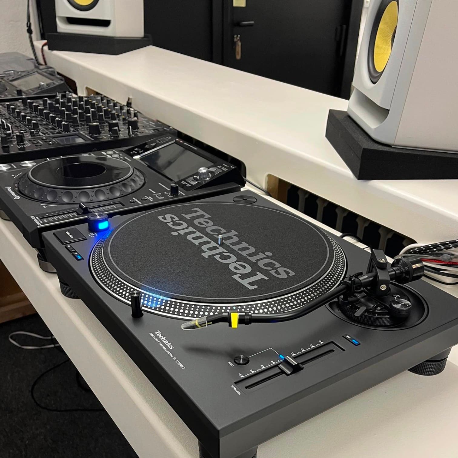 Platan Technics SL-1210MK7 pe un pupitru DJ, cu player și mixer în fundal